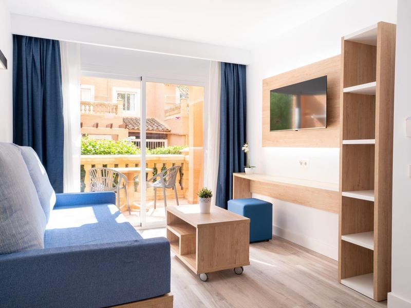 Jasny salon z niebieską sofą, meblami drewnianymi i balkonem z widokiem na sąsiednie budynki.