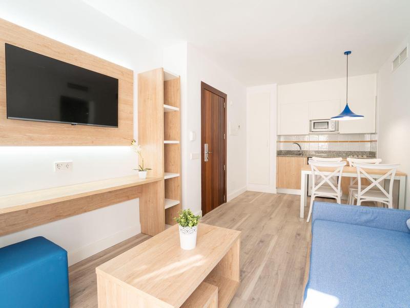 Nowoczesny salon z aneksem kuchennym, drewnianymi półkami i niebieską sofą w jasno urządzonym apartamencie wakacyjnym.