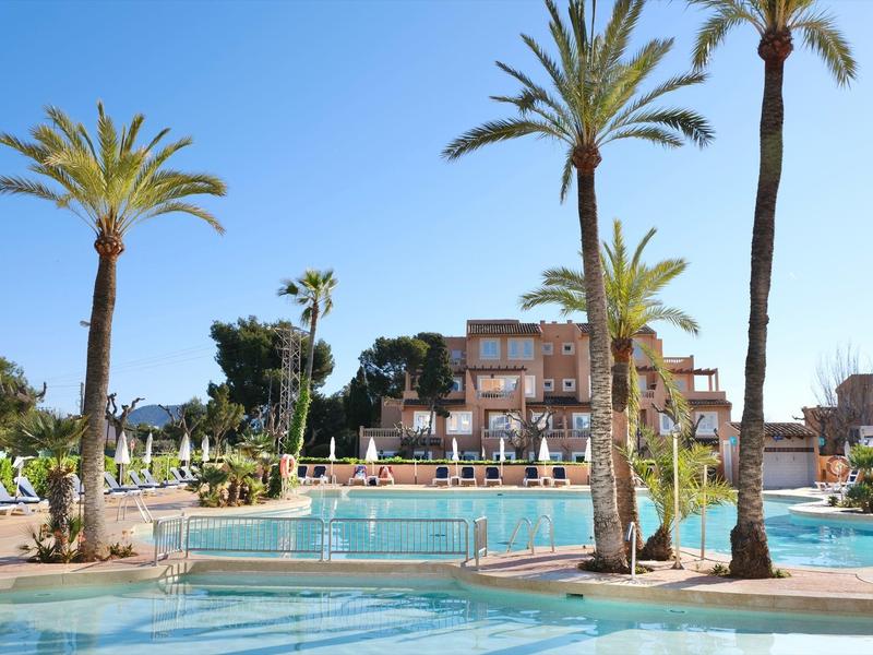 Duży basen hotelowy z leżakami i palmami pod czystym niebem.