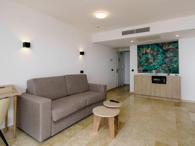 Moderner Wohnraum mit grauem Sofa, zwei kleinen runden Tischen, Holzkommode und grünem Wandkunstwerk.