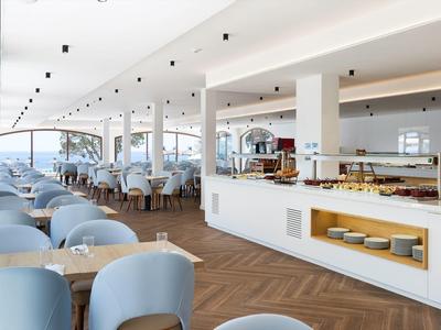 Hell gestalteter, moderner Speisesaal mit blauen Stühlen, Holzboden und Buffetbereich.