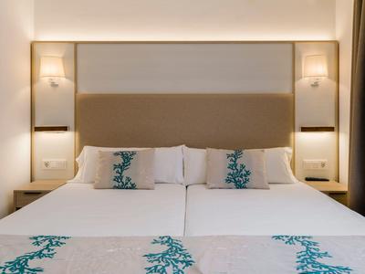 Cama doble moderna con ropa de cama blanca y azul en una habitación de hotel bien iluminada.