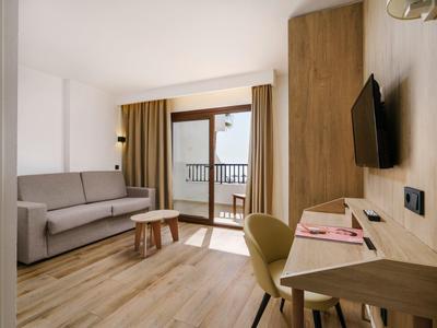 Modernes Wohnzimmer mit grauer Couch, Holzmöbeln, Schreibtisch, Stuhl und Balkon mit Aussicht.