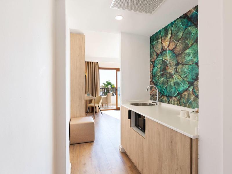 Área de cocina de habitación de hotel moderna con gabinetes de madera y acento de pared de mosaico verde.