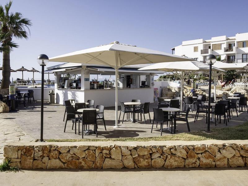 Área exterior de un hotel con sombrillas y mesas cerca del mar.