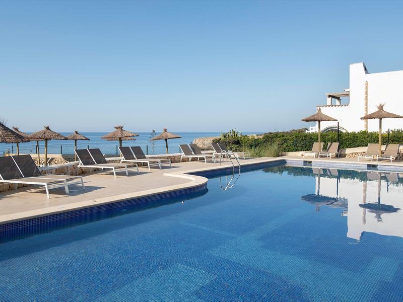 Piscina junto al mar con tumbonas y sombrillas en un hotel bajo un cielo despejado.