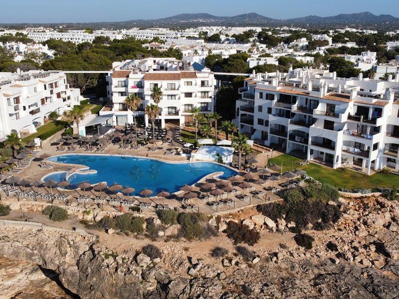 Complejo hotelero con grandes piscinas, terrazas y edificios blancos en un paisaje costero rocoso.