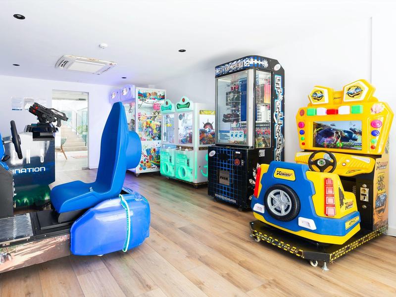 Zona de juegos para niños con arcade y simulador con asientos azules sobre suelo de madera.