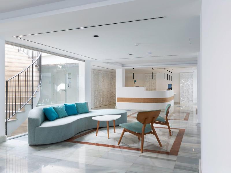 Recepción moderna de hotel con sofá curvo azul, sillas de diseño y mostrador blanco minimalista.