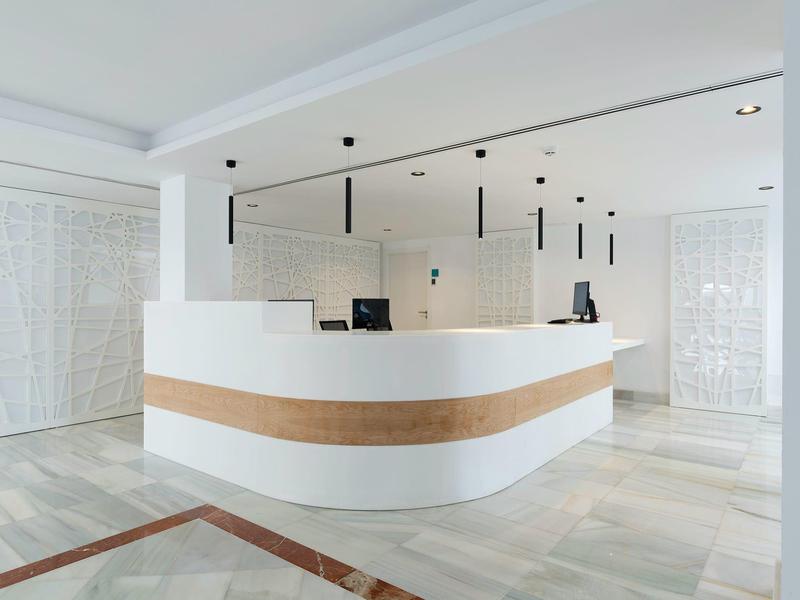 Recepción moderna de hotel con mostrador curvo blanco y iluminación minimalista.