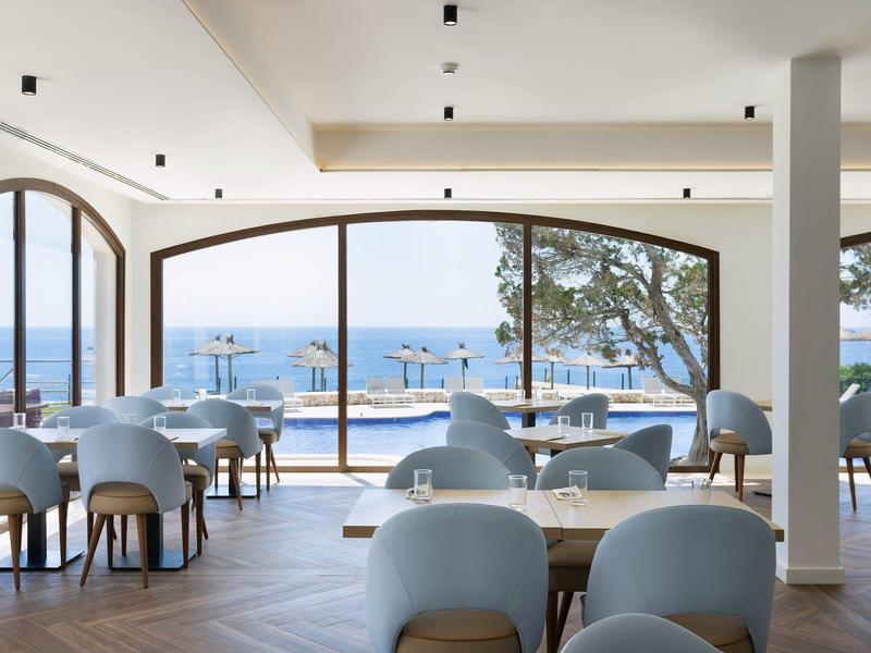 Zona de comedor moderna en hotel con grandes ventanales y vista al mar, con asientos en terraza.