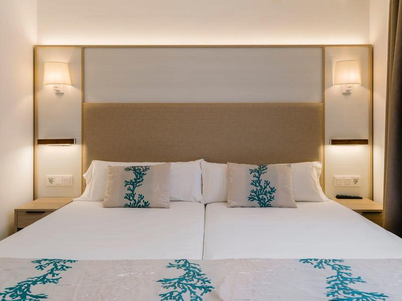 Cama doble moderna con ropa de cama blanca y azul en una habitación de hotel bien iluminada.