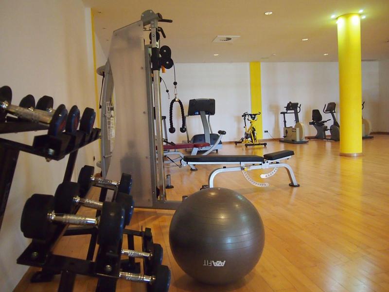 Salle de sport moderne avec divers équipements d'entraînement et sol en bois clair.