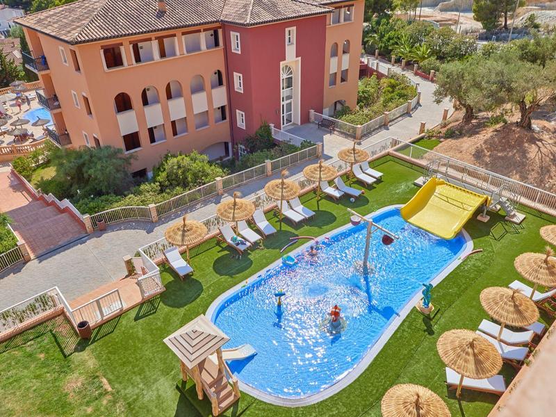 Espace piscine avec parasols, transats et toboggan à côté d'un bâtiment hôtelier.