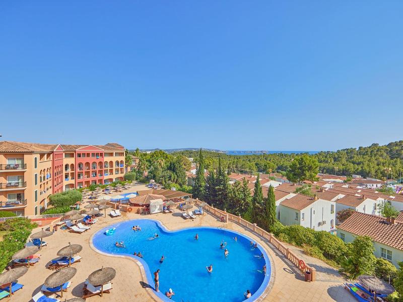 Grand piscine extérieure avec transats et bâtiments environnants sous un ciel bleu clair.