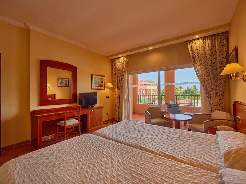 Chambre d'hôtel avec deux lits simples, bureau, TV et balcon avec vue.