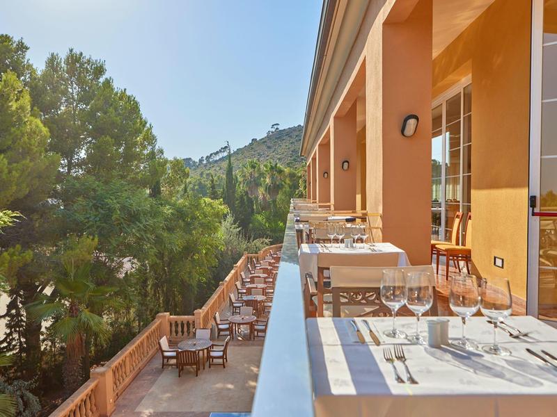 Terrasse avec des tables dressées à côté d'un hôtel surplombant des arbres verts et des collines.