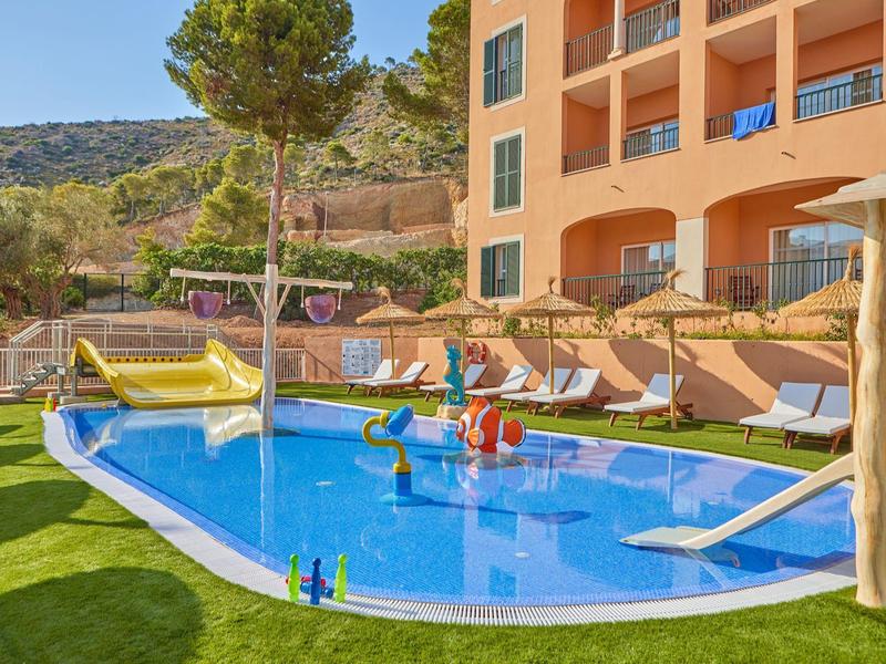 Petit bassin avec toboggan gonflable et chaises longues dans le jardin de l'hôtel par une journée ensoleillée.