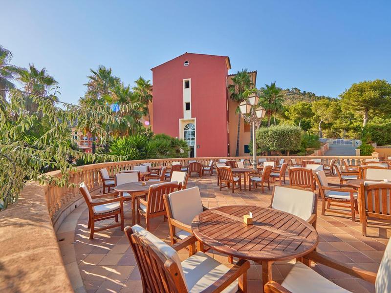 Terrasse avec tables et chaises en bois devant un bâtiment rouge sous un ciel bleu.