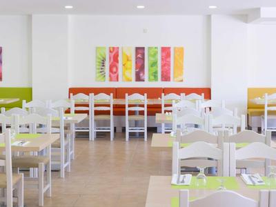 Helles, modernes Restaurant mit weißen Stühlen, bunten Wandbildern und gelben, orangefarbenen Sitzbänken.
