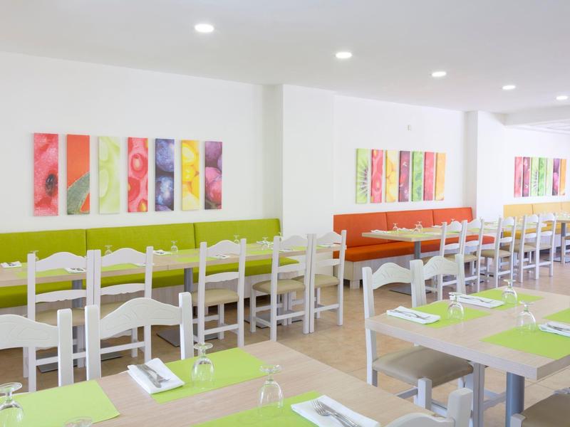 Salle à manger lumineuse avec chaises blanches, sets de table colorés et tableaux abstraits aux murs.