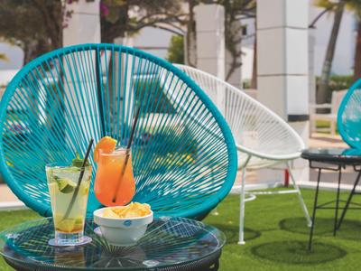 Dva osvěžující nápoje a občerstvení na stole před barevnými venkovními židlemi.