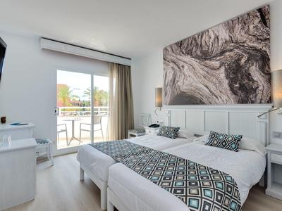 Nowoczesny pokój hotelowy z podwójnym łóżkiem, wzorzystymi poduszkami, balkonem i jasnym światłem naturalnym.