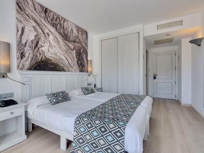 Nowoczesny pokój hotelowy z dwoma pojedynczymi łóżkami, drewnianą podłogą i abstrakcyjną grafiką na ścianie.