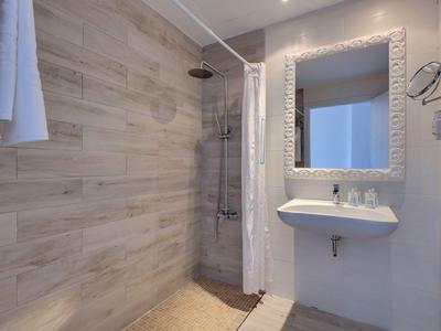 Nowoczesna łazienka hotelowa z prysznicem typu walk-in, białą umywalką i dużym lustrem z oświetleniem.