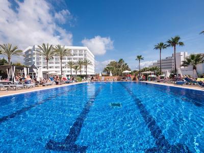 Duży basen na świeżym powietrzu w słonecznym kurorcie z palmami i leżakami.