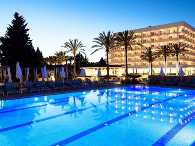 Luksusowy hotel z jasno oświetlonym basenem i palmami o zmierzchu.