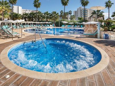 Okrągła, bąbelkowa jacuzzi obok dużego basenu z palmami w słonecznym kurorcie.