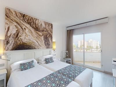 Jasny pokój hotelowy z podwójnym łóżkiem, nowoczesnym wystrojem i balkonem z widokiem na miasto.