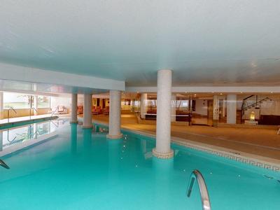 Hotelowy basen kryty z czystą wodą, białe kolumny i strefa wypoczynkowa w tle.