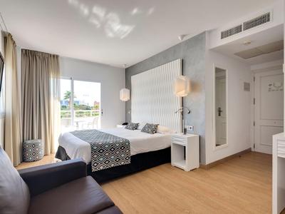 Jasny pokój hotelowy z podwójnym łóżkiem, sofą, drewnianą podłogą i dużym oknem z zasłonami.