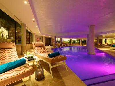 Piscine intérieure avec éclairage violet et chaises longues confortables avec serviettes bleues.