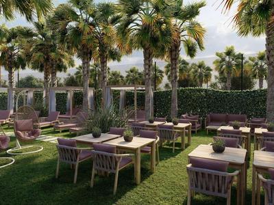 Espace extérieur d'hôtel avec tables, chaises et palmiers tropicaux sur gazon.