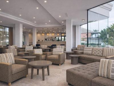 Espace lounge d'hôtel moderne avec fauteuils, canapés et grandes fenêtres.