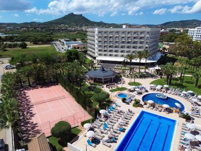 Hôtel avec piscine, court de tennis et jardin dans un paysage verdoyant.