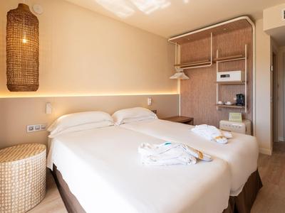 Modern hotel room with two single beds, warm lighting, and minimalist design.