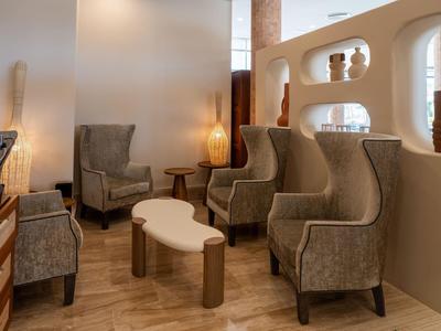 Cozy seating area with four beige armchairs and two white tables on wooden floor in hotel setting.
