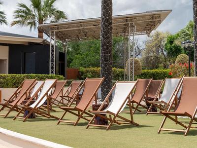 Plusieurs chaises longues en bois et tissu sont disposées sur de l'herbe artificielle près d'une zone d'hôtel.