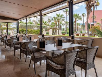 Espace extérieur couvert avec tables et chaises entouré de palmiers dans un jardin d'hôtel.