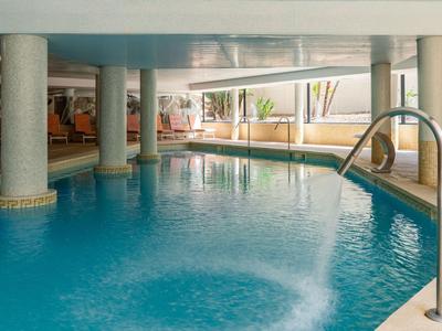 Indoor hotel pool with columns, blue water surface, and natural light through windows.