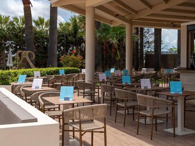 Covered hotel terrace with tables and chairs, set with blue menu boards.