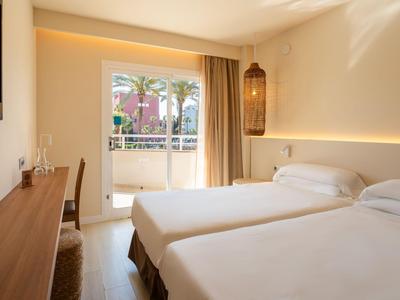 Bright hotel room with two single beds, balcony, and modern lighting.