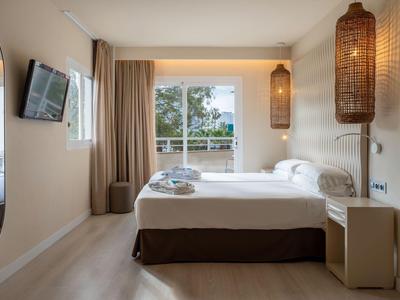 Bright hotel room with a double bed, large windows, and modern wall lamps.