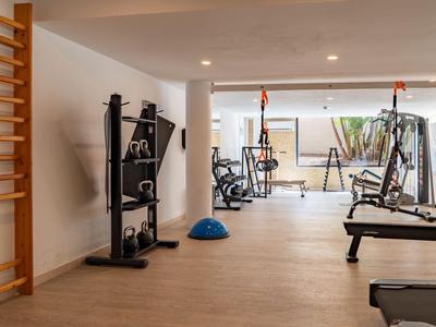 Modern gym with various exercise equipment and large windows overlooking greenery.
