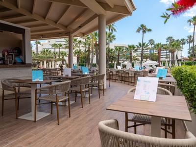 Open hotel terrace area with tables and chairs under a wooden roof.