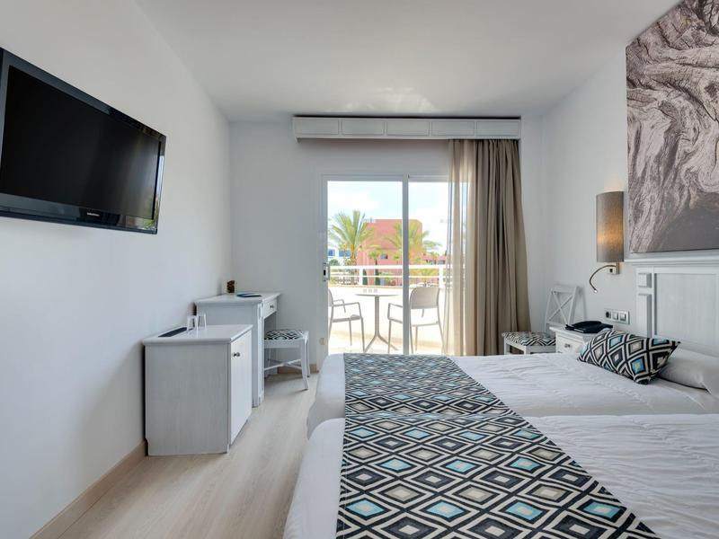 Jasny, nowoczesny pokój hotelowy z dwoma łóżkami, telewizorem, biurkiem i balkonem.